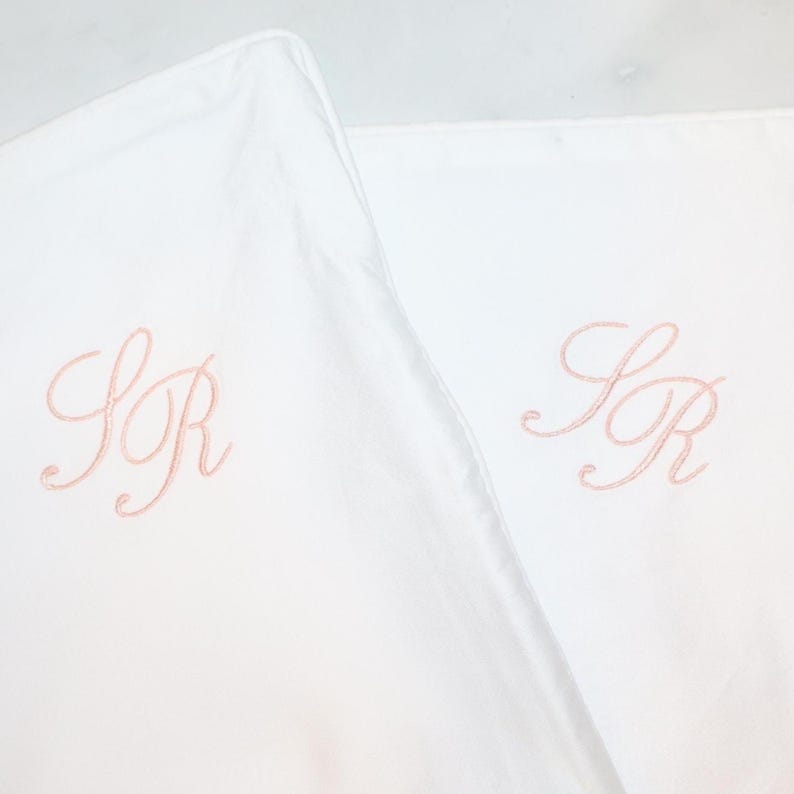 Two white pillowcases are shown, each embroidered with the intertwined pink script initials "SR".
