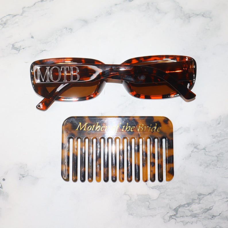 K&ouml;nnte beinhalten: Sonnenbrille im Schildpatt-Design mit dem Text "MOTB" und ein passender Kamm mit der Aufschrift "Mother of the Bride". Die Sonnenbrille hat braune Gl&auml;ser und der Kamm hat ein klassisches Design.
