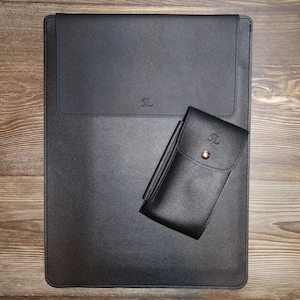 Könnte beinhalten: Eine schwarze Laptophülle aus Leder und eine passende kleinere schwarze Ledertasche mit silbernem Druckknopfverschluss. Beide Artikel tragen den geprägten Text 5L auf der Vorderseite. Die Hülle hat ein rechteckiges Klappendesign mit Nähten.