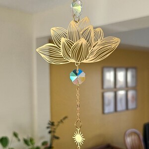 May include: Gold-toned metal lotus flower suncatcher with iridescent crystal beads and a large teardrop-shaped crystal hanging from the bottom.