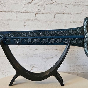 May include: A dark blue sword with intricate leaf designs on the blade, displayed on a black stand. The sword has a silver-colored hilt and a black handle.