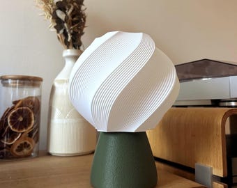 May include: A table lamp featuring a white, spherical shade with a distinct spiraling, ribbed texture. The base of the lamp is a solid, matte, dark olive green truncated cone with a textured surface finish, providing a stable foundation.