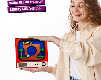 May include: A red and black retro television with a screen showing a pixelated image of Sonic the Hedgehog running through a level. The text "SONIC THE HEDGEHOG" is visible on the screen. The television is being held by a person's hands.