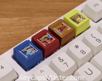 May include: Four miniature game cartridges, resembling classic Nintendo Game Boy cartridges, are placed on a white keyboard. The cartridges are blue, red, gold, and yellow, and feature the Pokemon logo and characters. The keyboard has white keys with black lettering.