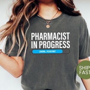 May include: A dark gray t-shirt with the text "Pharmacist in Progress" and a blue progress bar that says "Loading... Please Wait".