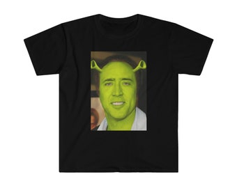Peut inclure: Un t-shirt noir à manches courtes avec une impression graphique rectangulaire centrale. L'image montre une personne à la peau verte avec deux oreilles vertes en forme de trompette dépassant de chaque côté de la tête, rappelant un ogre.