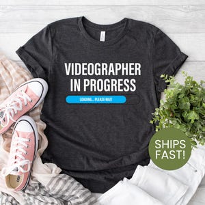May include: A dark grey t-shirt with the text "Videographer in Progress" and a blue progress bar that says "Loading... Please wait".