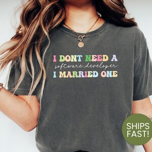 May include: A dark gray t-shirt with the text "I don't need a software developer I married one" in rainbow colors.