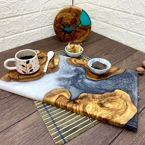May include: A wooden serving board with a white and gray resin design, accompanied by a small cup of coffee, a spoon, and small bowls. A round wooden piece with blue resin is in the background. Walnuts are scattered around.