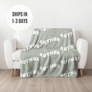 May include: A soft, sage green throw blanket with a white repeating pattern of the word "AUTHOR" in a retro, bubbly font.