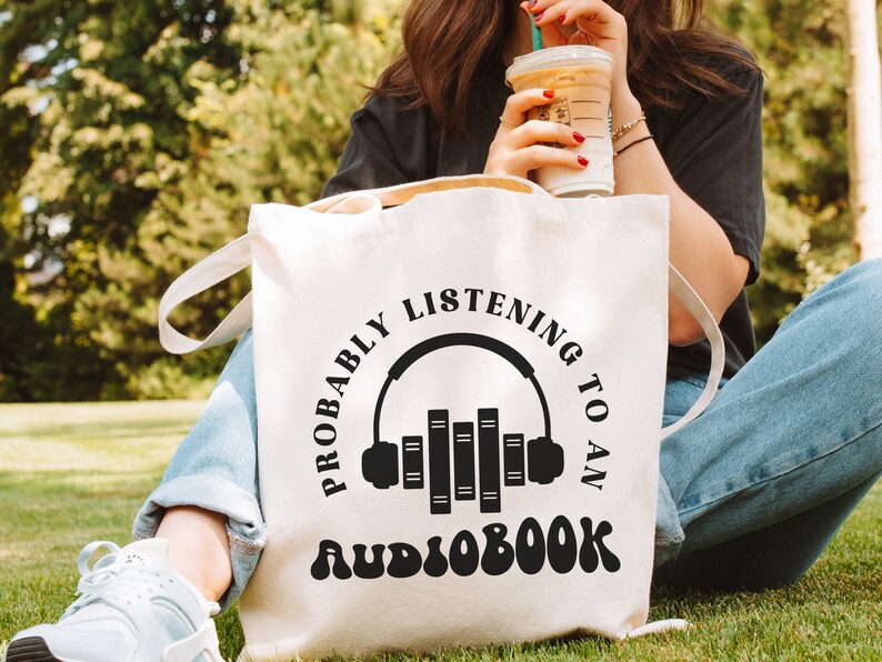 May include: White canvas tote bag with black text that reads "Probably listening to an audiobook" with a graphic of headphones and books.