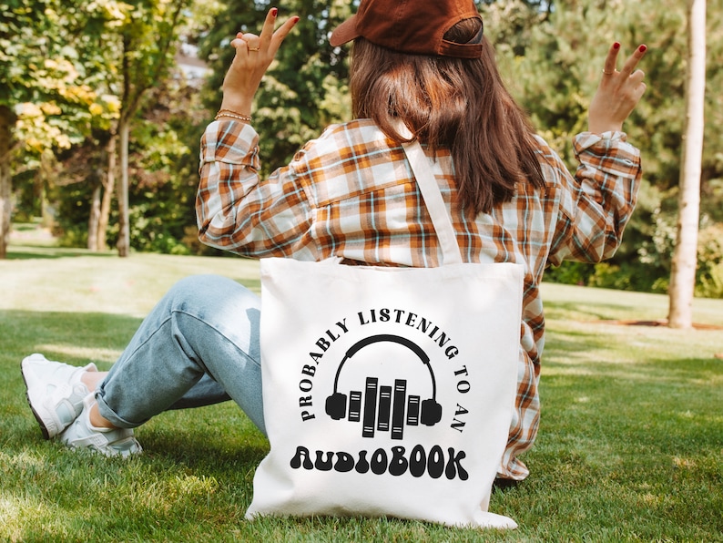 May include: A white tote bag with a black graphic that says "Probably listening to an audiobook" with a stylized image of headphones and books.
