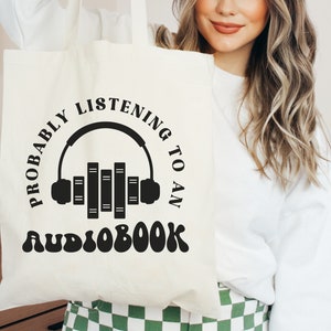May include: White tote bag with black text that reads "Probably listening to an audiobook" with a graphic of headphones and books.