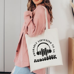 May include: White tote bag with black text that reads "Probably listening to an audiobook" with a graphic of headphones and books.