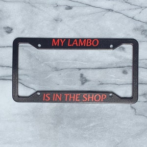 May include: Black license plate frame with red text that reads "MY LAMBO IS IN THE SHOP".