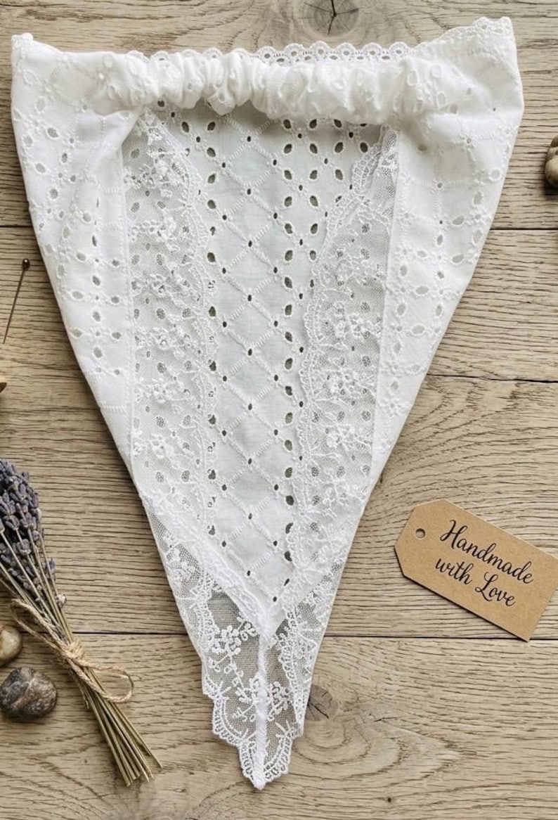 May include: White, triangular-shaped eyelet fabric with a scalloped edge. The fabric has a diamond pattern with small holes and floral lace details. A tag that says "Handmade with Love" is visible.