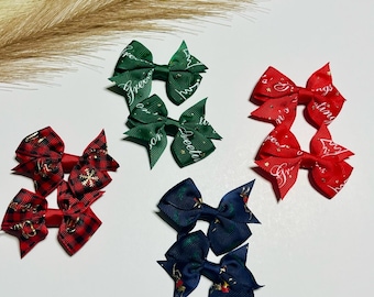 Puede incluir: Conjunto de seis lazos para el pelo con temática navideña. Dos lazos verdes con texto blanco que dice "Feliz Navidad", dos lazos rojos con texto blanco que dice "Felices Fiestas", y dos lazos de cuadros rojos y negros con un diseño de copo de nieve.