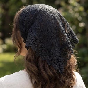 May include: A black lace head covering featuring a floral pattern and a scalloped edge. The triangular fabric piece is draped over the top of the head, with the intricate lace design covering the hair and extending down to the nape of the neck.