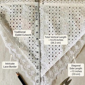 May include: White eyelet cutwork fabric with an intricate lace border. The total top width is approximately 16 inches (40.6 cm), with a vertical length of about 14.25 inches (36.2 cm). The diagonal side length is about 13 inches (33 cm). A pencil and scissors are also in the image.