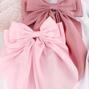 May include: Two large satin bows, one pink and one dusty rose, with long tails. The bows are tied together and are on a white background.