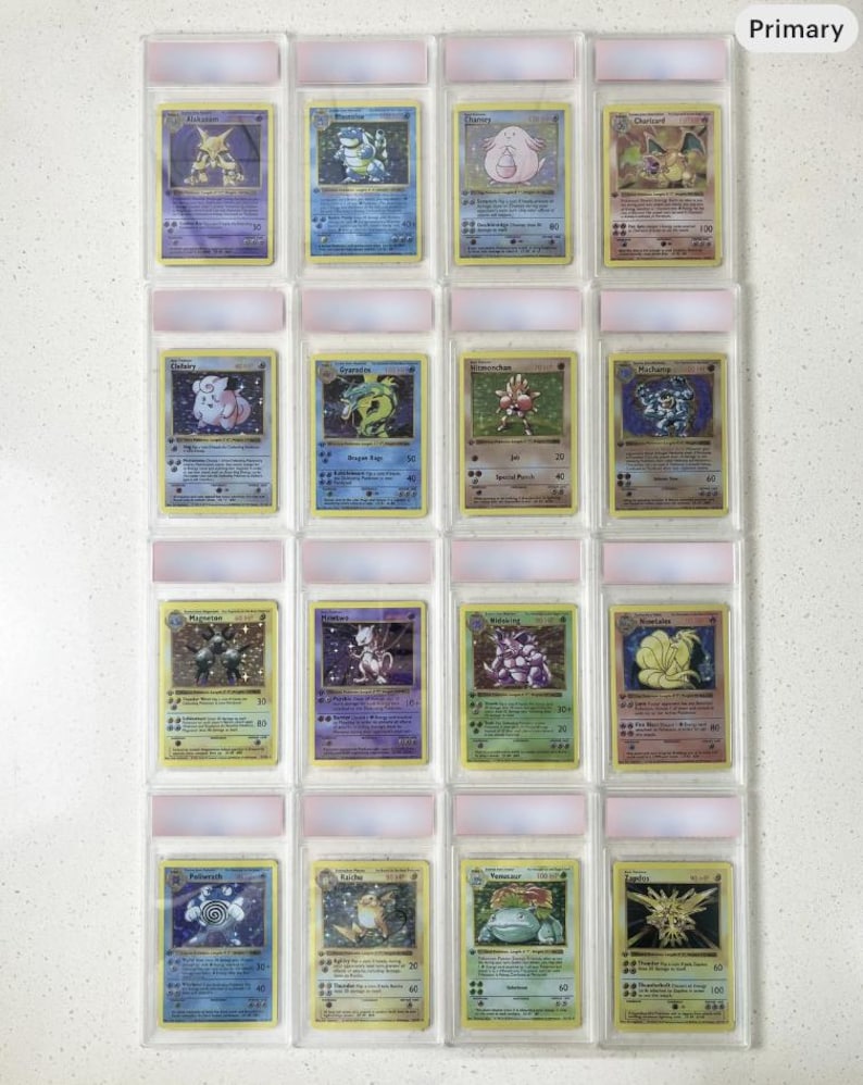 May include: A collection of sixteen Pokemon trading cards, each encased in a protective plastic sleeve. The cards feature various colorful illustrations of Pokemon characters, with text and symbols. The cards are arranged in four rows of four.