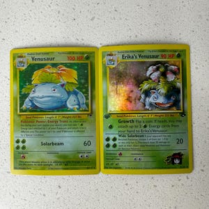 May include: Two Pokémon trading cards featuring Venusaur. The first card shows Venusaur with 100 HP and the Solarbeam attack. The second card is Erika's Venusaur with 90 HP and the Growth attack. Both cards have a green and yellow color scheme.