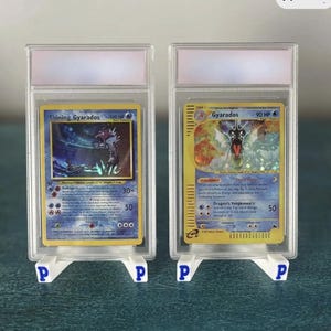 May include: A white ceramic mug with a black handle and the text "But First, Coffee" in a bold, black font. The mug is filled with a dark liquid, likely coffee, and sits on a light-colored surface.