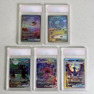 May include: Five collectible trading cards in clear protective cases. The cards feature colourful illustrations of various characters and creatures. Each card has a unique design and is encased in a rigid plastic holder with a white label at the top.