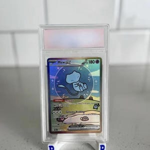 May include: A graded Pokémon trading card featuring Mew ex. The card has a holographic design with a blue Mew illustration and the number 180. The card is encased in a clear plastic holder and displayed on a white stand.