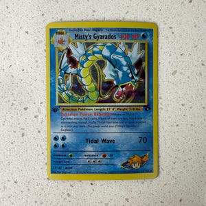 May include: A vintage Misty's Gyarados Pokémon trading card. The card features a blue and yellow serpentine creature with the text "Misty's Gyarados" and "100 HP". The card measures 21' 4" in length and weighs 518 lbs.