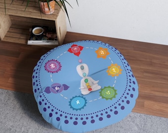 Op de afbeelding: Een blauw rond vloer kussen met een wit figuur dat in het midden zit. Het figuur heeft een regenboogontwerp en is omringd door zeven kleurrijke cirkels met Sanskriet-symbolen. Het kussen heeft een blauwe achtergrond met een patroon van witte stippen.