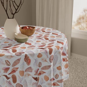 May include: A round tablecloth with a seashell pattern in shades of brown, peach, and white. The table is set with a white vase, a woven basket, and two bowls. The tablecloth features various seashell illustrations.
