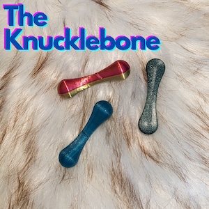 May include: Three knucklebone toys. One is a dark blue, one is a light blue, and one is a pink and gold color.
