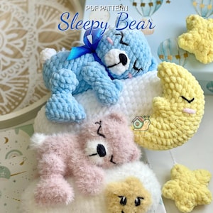 May include: Crocheted baby mobile featuring a blue bear with a blue ribbon, a pink bear, a yellow crescent moon, and yellow stars. The text "Sleepy Bear" is displayed at the top. The items are on a white cloud.