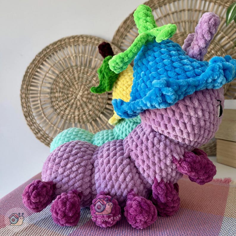 Puede incluir: Un juguete de oruga de ganchillo hecho a mano en tonos de morado, azul, verde y amarillo. La oruga tiene un dise&ntilde;o caprichoso con un sombrero grande y colorido y m&uacute;ltiples patas. El juguete est&aacute; hecho de hilo suave y afelpado y est&aacute; dise&ntilde;ado para ni&ntilde;os.