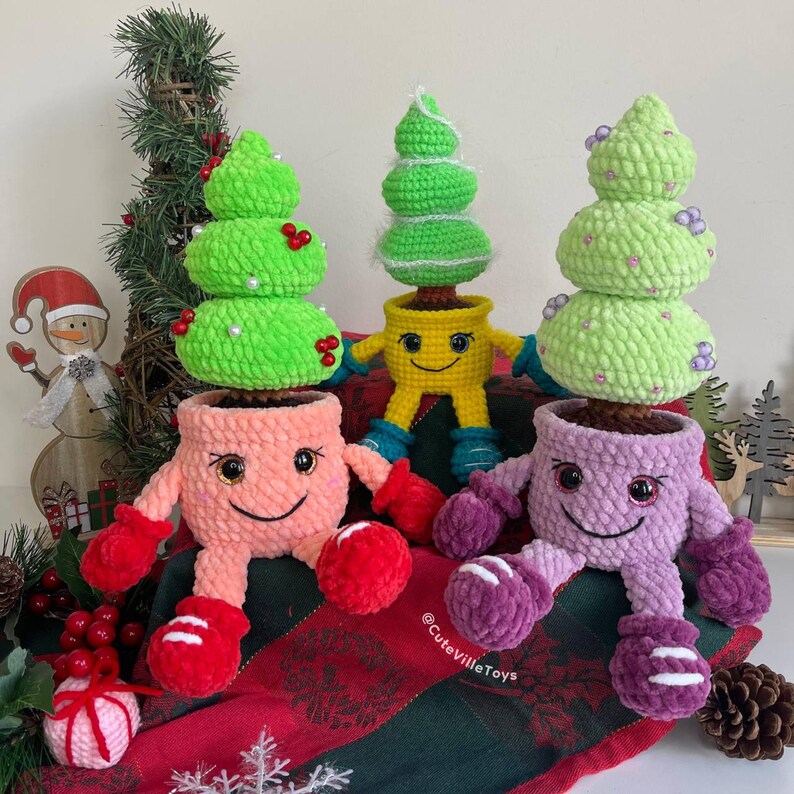 Three crochet Christmas trees with varied decorations and shades of green in smiling pots, arranged in different positions to showcase their unique styles and details.