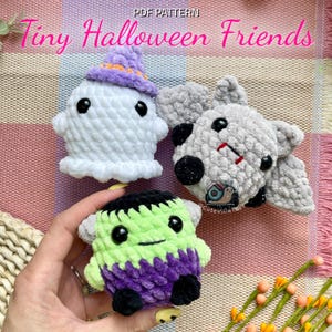 May include: Three handmade crochet Halloween toys: a white ghost with a purple hat, a grey bat, and a green and purple Frankenstein's monster. The text "Tiny Halloween Friends" is at the top. The toys are made of soft, textured yarn.