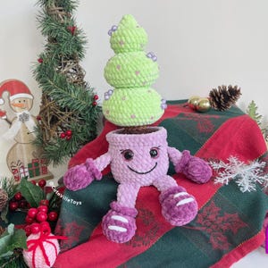 Christmas tree in smiling pot made in different colors: light purple pot with purple mittens and boots. The tree is decorated with colorful beads.