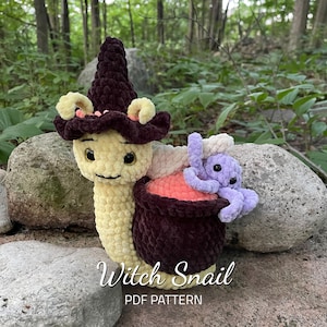 May include: A crocheted witch snail with a purple octopus in its shell. The snail is wearing a brown witch hat with a pink flower detail. The snail and octopus are sitting on a rock with a green background.
