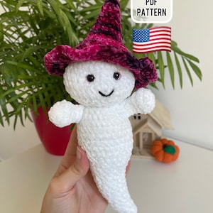 Op de afbeelding: Een witte gehaakte geest die een roze en zwarte fluwelen heksenhoed draagt. De geest heeft zwarte ogen en een glimlachende mond. De afbeelding bevat de tekst "PDF PATTERN" en een kleine Amerikaanse vlag.