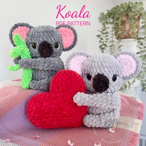 May include: Two grey crocheted koala plushies. One koala is holding a green crocheted eucalyptus branch. The other koala is holding a red crocheted heart. The text "Koala PDF Pattern" is above the plushies.