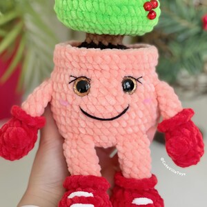 Close-up of a crochet Christmas tree showing pot details: eyes, eyelashes, cheeks, and mouth.