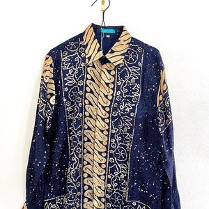 Peut inclure: Une chemise à manches longues bleu marine avec un motif batik doré. La chemise a un col boutonné et une coupe décontractée.