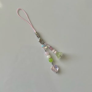 Peut inclure: Un porte-cl&eacute;s de t&eacute;l&eacute;phone rose avec un cristal en forme de c&oelig;ur, des perles vertes et roses et un charme de fleur.