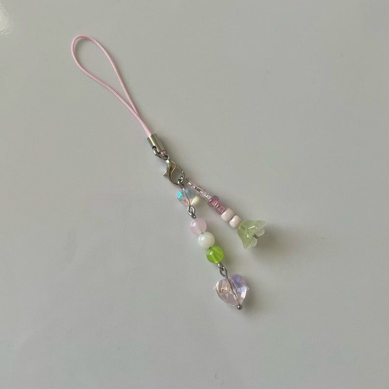 Peut inclure: Un porte-cl&eacute;s de t&eacute;l&eacute;phone rose avec un cristal en forme de c&oelig;ur, des perles vertes et roses et un charme de fleur.