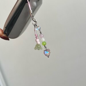 Peut inclure: Un porte-cl&eacute;s de t&eacute;l&eacute;phone en perles roses et vertes avec un cristal en forme de c&oelig;ur et des breloques en forme de fleurs.