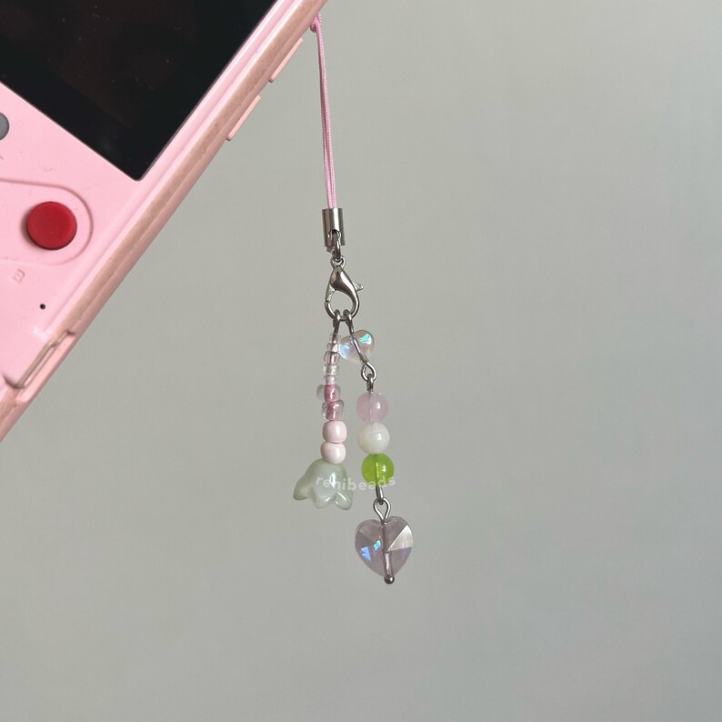 Peut inclure: Un charme en perles roses et vertes avec un charme en cristal en forme de c&oelig;ur au bas. Le charme est attach&eacute; &agrave; une ficelle rose et un fermoir argent&eacute;.