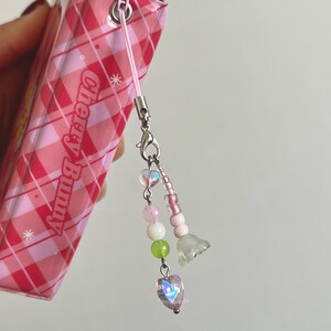 Peut inclure: Un carnet &agrave; carreaux rose et blanc avec un charme en perles rose et blanc attach&eacute;. Le charme comprend un cristal en forme de c&oelig;ur, des perles rose et blanc et deux petits charmes en forme de fleur. Le carnet porte l'inscription "Cherry Bunny" sur la couverture.