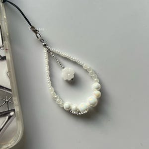 May include: White phone charm with a four-leaf clover charm and iridescent white beads.