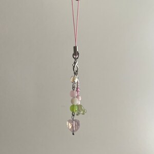 Peut inclure: Un porte-cl&eacute;s de t&eacute;l&eacute;phone en perles roses et vertes avec un charme en forme de c&oelig;ur au bas. Le charme est attach&eacute; &agrave; une ficelle rose.